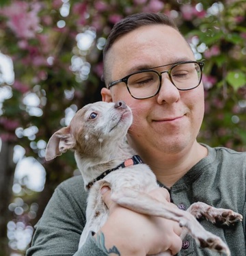 Mann mit Brille hält einen kleinen Hund und lächelt, während er die Augen geschlossen hat