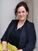 Katrin Terwiel sitzt an ein Gebäude gelehnt und lächelt.