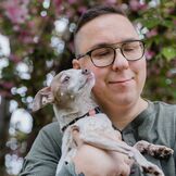 Mann mit Brille hält einen kleinen Hund und lächelt, während er die Augen geschlossen hat